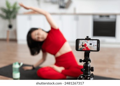 Woman in red activewear filming yoga session at home with smartphone. Focus on phone screen displaying stretching exercise. Home workout, fitness routine, and online yoga class. - Powered by Shutterstock