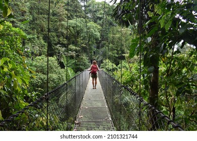 A woman with a red backpack exploring the lush jungle in Costa Rica over an adventurous hanging bridge.