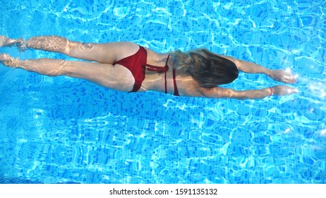 Woman In Red Bikini Diving In Pool And Splashing Crystal Clear Water. Sexy Girl Swimming Under Water In Basin Of Hotel At Sunny Day. Elegant Lady Relaxing On Tropical Resort During Vacation. Top View