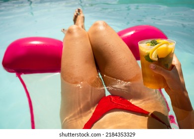 Woman in red bikini on a inflatable mattress having a mojito cocktail inside the swimming pool in summer