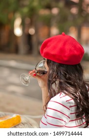 Woman In A Red Cap Drinking Red Wine In Outdoor Cafe