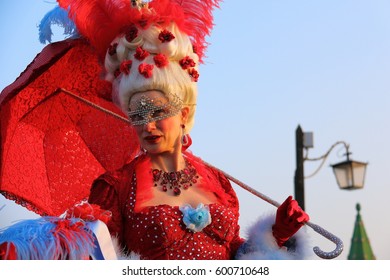 A Woman In A Red Carnival Costume Of Marie Antoinette And A Mask Holds A Red Umbrella On The Embankment In Venice Italy, February 20, 2017