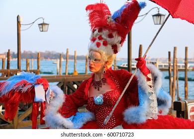 A Woman In A Red Carnival Costume Of Marie Antoinette And A Mask Holds A Red Umbrella On The Embankment In Venice. Venice Italy, February 20, 2017