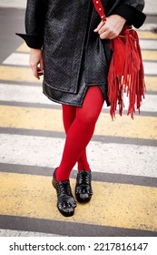 Woman in red color tights, black shoes with rivets and hand bag with fringe standing on pedestrian crossing. Fashion details for stylish extravagant women