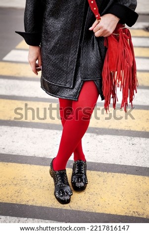 Woman in red color tights, black shoes with rivets and hand bag with fringe standing on pedestrian crossing. Fashion details for stylish extravagant women