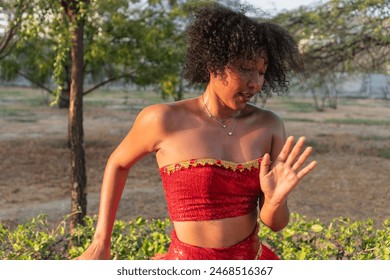 Woman in red costume dancing in outdoor park setting, curly hair, expressive movement. - Powered by Shutterstock