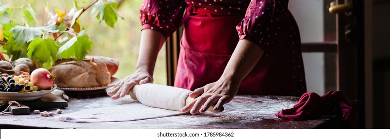 Woman In Red Dress And Apron Is Preparing A Dough For Delicious Homemade Pink Pasta On Her Kitchen. Dark And Moody, Low Key. Green Background. Italy, Tuscany. Banner