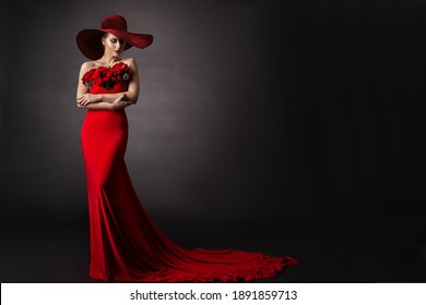 Woman Red Dress And Hat. Fashion Model In Long Evening Gown With Flowers. Black Studio Background.