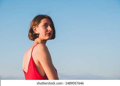 Woman in red dress looking back behind the shoulder  Young female in evening dress in rising sun outdoors  spontaneous real life portrait