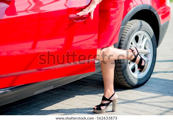 A woman in a red dress near the red car.\
Visible to the lower part of the\
body.