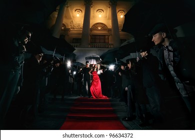 woman in red dress posing in front of paparazzi