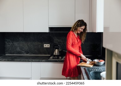 woman in a red dress prepares a salad in the kitchen - Powered by Shutterstock