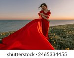 woman red dress standing grassy hillside. The sun is setting in the background, casting a warm glow over the scene. The woman is enjoying the beautiful view and the peaceful atmosphere.