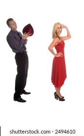 A Woman In A Red Dress Throws Her Mans Gift Of A Heart Shaped Box Of Chocolates Back Over Hr Shoulder To The Man Standing Behind Her