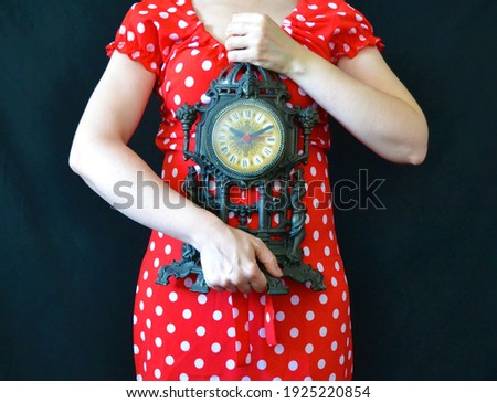 Woman in a red dress with white polka dots holding a clock on a black background
