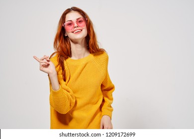 woman in red glasses and yellow sweater shows her finger to the side                         