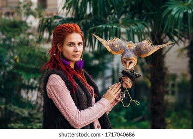 Woman with red hair holding owl in her hands. Hippie style. Palm tree on background.