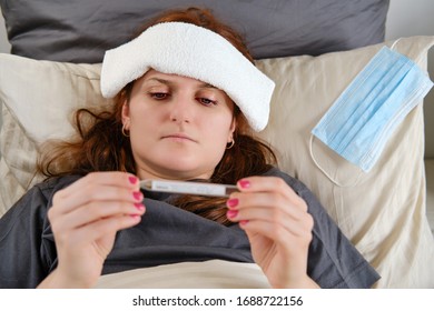 Woman With Red Hair Lies In Bed Sick With Coronavirus With A Cold Compress On Her Head