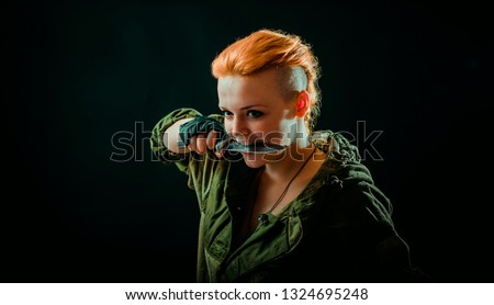 Woman with red hair in military uniform, keep a knife in her teeth