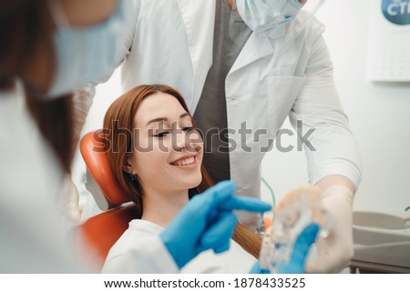 Woman with red hair sits in a dental chair while doctors demonstrate teeth cast.