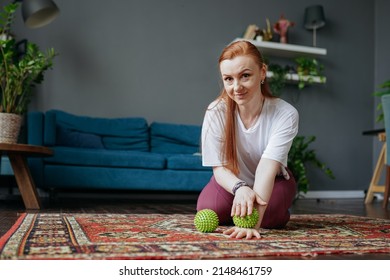 A Woman With Red Hair Sits On The Floor In The Living Room And Does A Myofascial Hand Massage With A Ball Looks At The Camera And Smiles