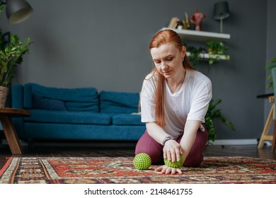 A Woman With Red Hair Is Sitting On The Floor In The Living Room And Doing A Myofascial Hand Massage With A Ball And Smiling