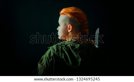 Woman with red hair stand back in military uniform, keep a knife in hand
