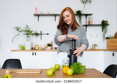 A Woman With Red Hair Is Standing In Her Kitchen Smiling And Cooking Celery Juice With A Juicer