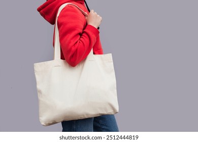 Woman in red hoodie holding tote canvas blank eco bag on street grey minimal wall background. Female consumer hold big white textile shopper. template or place for your design, text, logo - Powered by Shutterstock