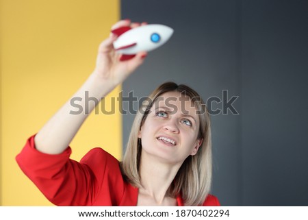 Woman in red jacket holding toy rocket above her head. Success in business development concept