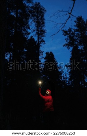 woman in red jacket in nature with flashlight or smartphone shines in dark. camping or picnic in the forest in mountains, solo hiking for person. twilight sunset.