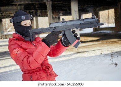 Woman In Red Jacket And Ski Mask Aiming With Gaming Gun Outdoor On Winter Day.