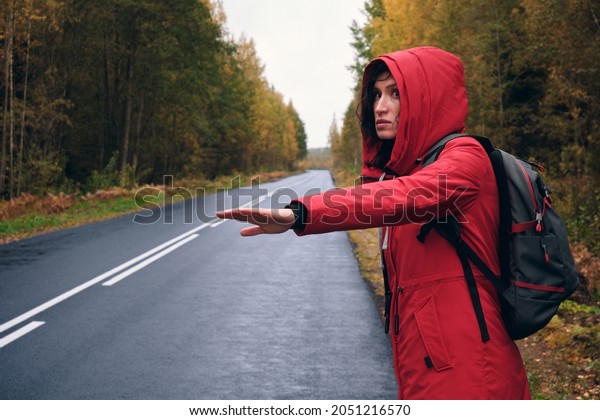 A Woman in a Red Jacket Trying to Stop a Car on the\
Forest Road.