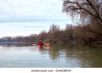 Woman in the red kayak rowing on the river on a cloudy calm winter day on the Danube River. Winter kayaking.