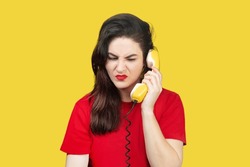 Woman With Red Lipstick Speaks On An Old Yellow Telephone With A Cord. Woman Is Unhappy, Does Not Want To Listen To Her Interlocutor, Gets Angry. Unwanted Call On A Yellow Background Isolated