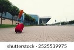 Woman with Red Luggage Walking Near Modern Airport Building. A rear view of a woman with long red hair pulling a bright red suitcase as she walks toward a modern airport building.