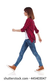 Woman In Red Lumberjack Shirt, Jeans And Brown Sneakers Walking And Looking Away. Side View. Full Length Studio Shot Isolated On White.