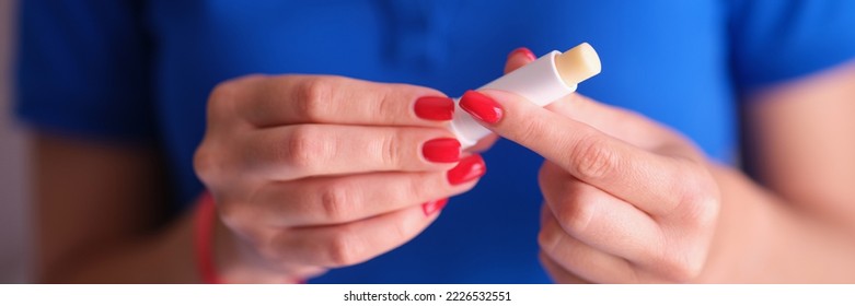 Woman with red manicure holding hygienic lipstick in hands closeup