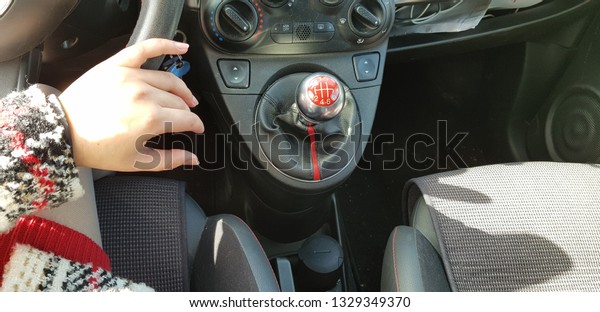 woman\
in red mini dress sitting on drivers seat of mini sport car holding\
her hand on steering wheel and passenger seat\
empty