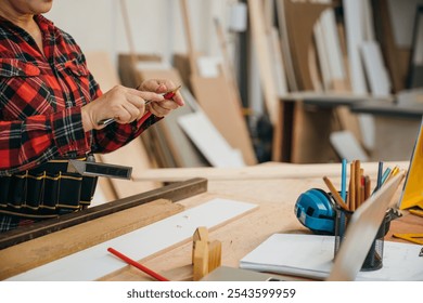 Woman in a red plaid shirt sharpening a pencil with a utility knife in a woodworking workshop. Ideal for carpentry, DIY projects, and banner displays with a focus on craftsmanship, Carpenter - Powered by Shutterstock