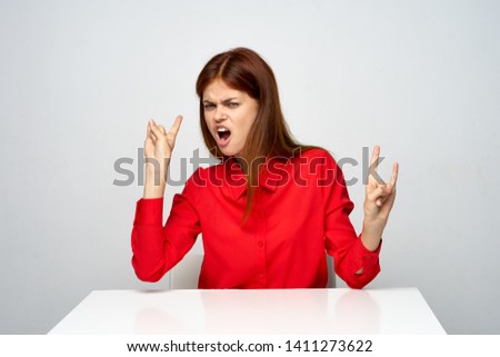 A woman in a red shirt at the table In a bright room, gesticulating with her hands and opened her mouth wide                   