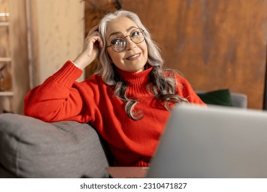 Woman in red shirt watching something on laptop - Shutterstock ID 2310471827