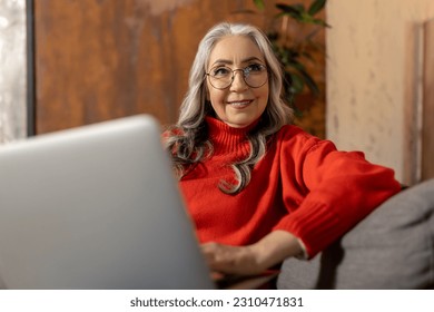 Woman in red shirt watching something on laptop - Shutterstock ID 2310471831