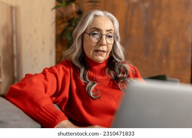 Woman in red shirt watching something on laptop - Shutterstock ID 2310471833