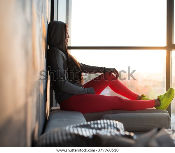 A woman in a red sport pants\
and in a yellow choes sitting near window and looking\
outside.