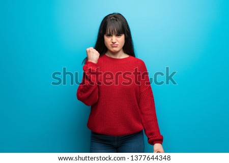 Woman with red sweater over blue wall with angry gesture