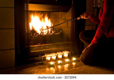 Woman in red sweater stoking a fire in the fireplace with candles burning in front