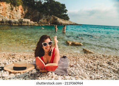 Woman In Red Swimsuit Laying On Blanket At Sea Beach Reading Book Sun Tanning