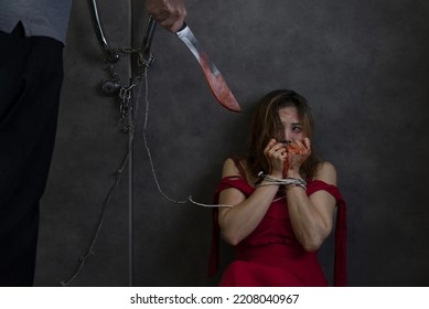 A Woman In Red Was Tied And Abused In A Dark Room, Intimidated By A Man Holding A Knife.concept Woman Victim, Crime, Violence, Hostage