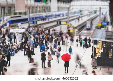 woman with red umbrella waiting at train station and blurred people in motion, solitude concept